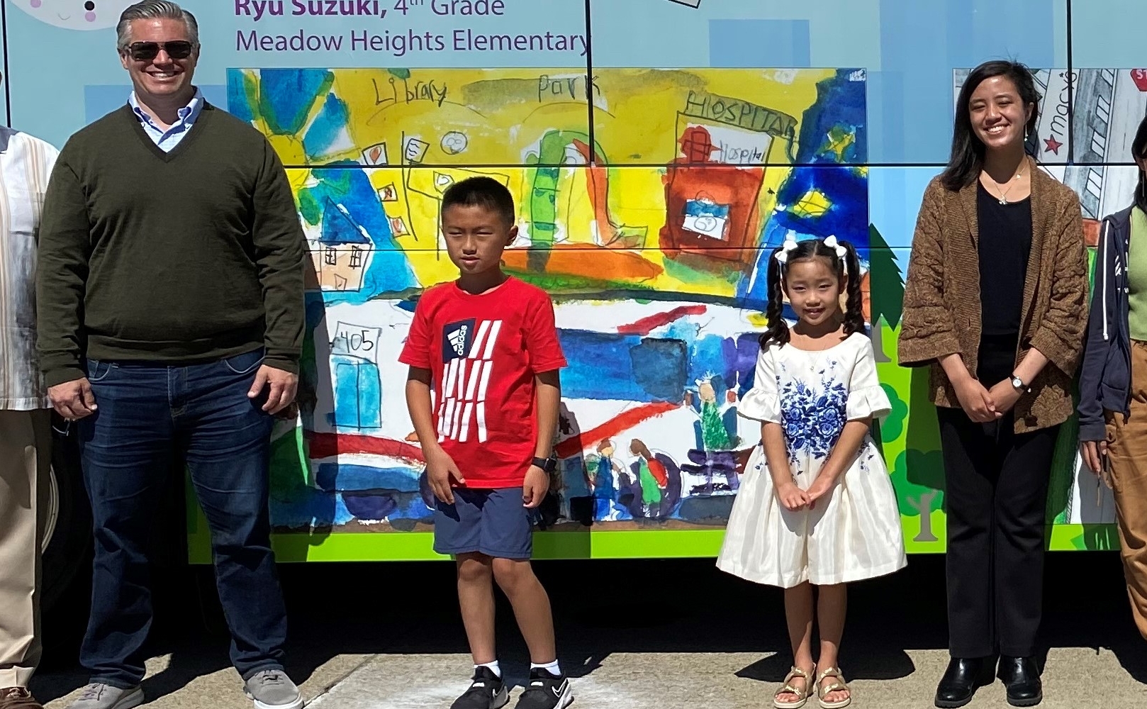 The winners of the Art Takes a Bus Ride Contest pose for a photo in front of a wrapped bus featuring their winning art