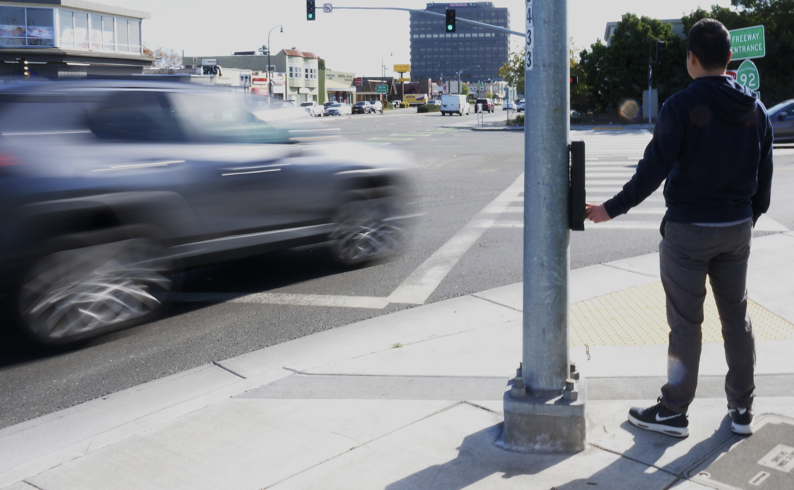 A pedestrian waits for traffic along a busy stretch of El Camino Real in San Mateo