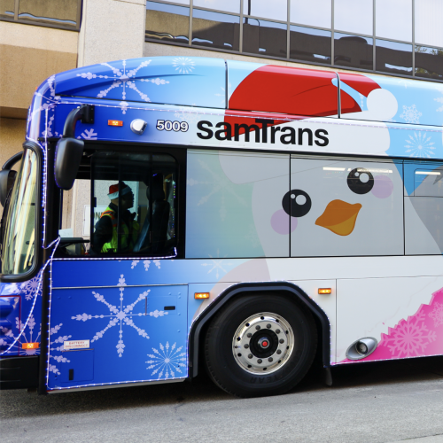 The SamTrans Holiday Bus with the Board of Directors and General Manager/CEO April Chan standing in front.